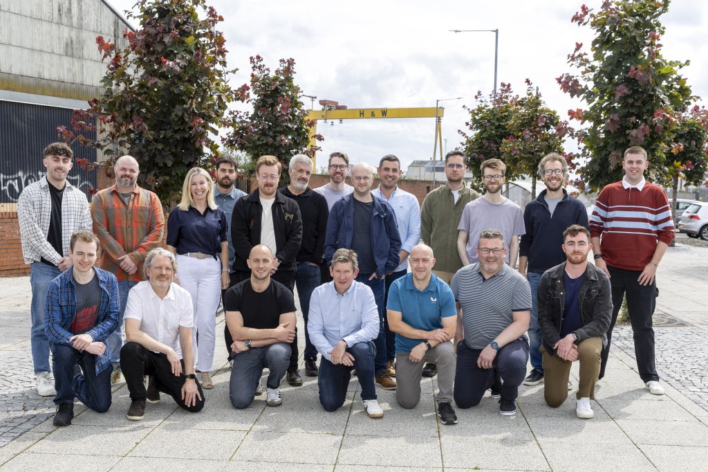 The CattleEye team gathered outdoors for a group photograph in Belfast's Titanic Quarter, with the iconic Harland & Wolff cranes visible in the background. The team stands and kneels together in bright daylight, reflecting the company's collaborative culture and Northern Ireland roots.